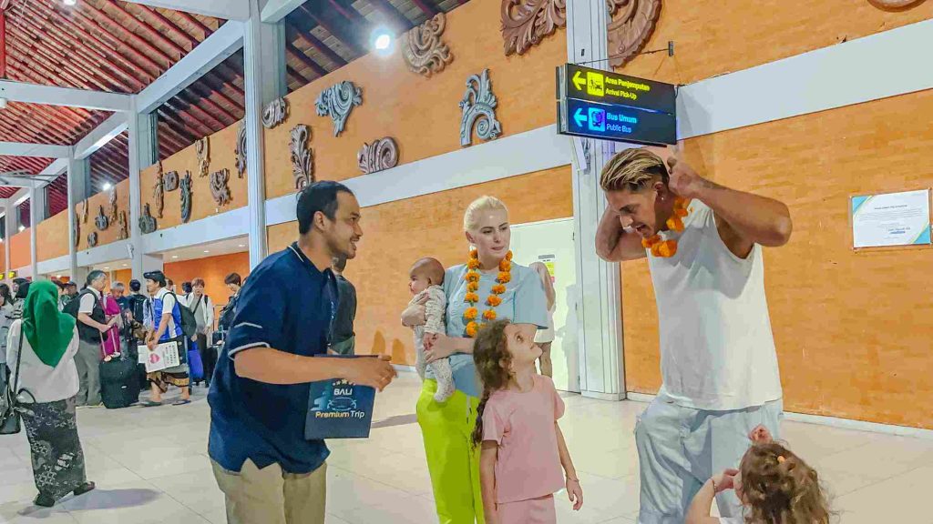 Bali Meet and Greet agent welcoming a family with flower garlands in the Ngurah Rai arrival hall